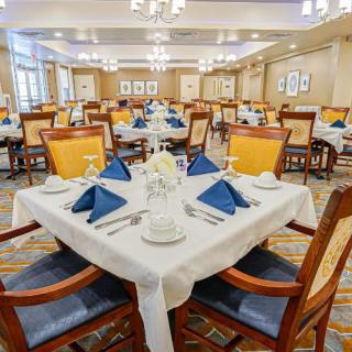 A well-set dining room with elegant tables and chairs, featuring blue napkins and neatly arranged place settings.