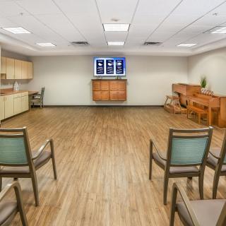 A well-lit meeting room with wooden floors, arranged with several chairs and a television mounted on the wall.