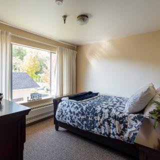 A cozy bedroom with a bed near a large window letting in sunlight.