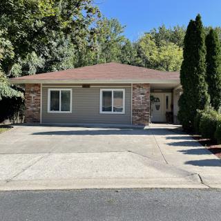 A charming single-story house with a well-maintained exterior and driveway surrounded by greenery.