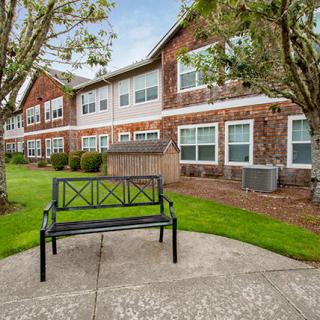 A bench sits in front of a brick building surrounded by trees and a well-maintained lawn.