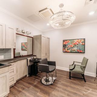A modern hair salon with stylish furnishings, featuring a chandelier and a large mirror.