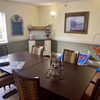 A cozy dining room with a large table and several chairs, decorated with artwork and shelves.