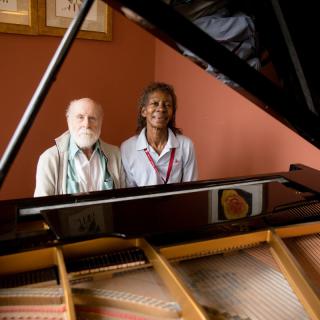 Two people sitting by a grand piano.