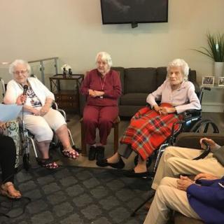 A group of elderly individuals sitting together in a living room setting, engaged in conversation.