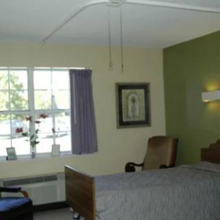 A hospital room featuring a bed, chair, window with curtains, and wall decor.