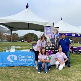 A group of volunteers at a community event, promoting services under a tent with the logo of Caretaker Keeper.