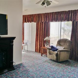 A cozy living room with an armchair next to large windows and a television above the fireplace.