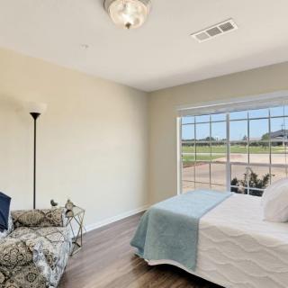 A minimalist bedroom with natural lighting, featuring a bed, lamp, and wooden flooring.