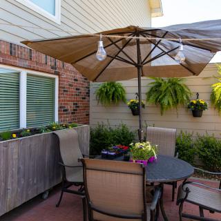 A cozy patio setup with a table and chairs under an umbrella, surrounded by hanging plants and flowers.