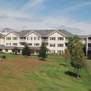 A residential apartment building surrounded by a large lawn and trees under a clear blue sky.