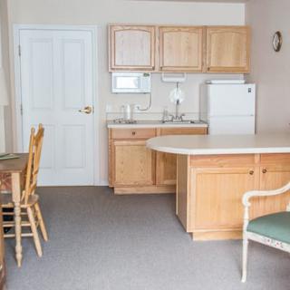 A simple kitchen interior with wooden cabinets, a refrigerator, and seating area.