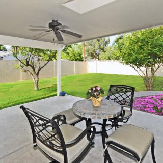 A cozy outdoor patio with a table and chairs, surrounded by a lush green garden.