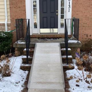 A ramp leading to the front entrance of a brick house with snow on the ground.