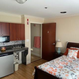 A compact studio apartment featuring a bed, kitchenette, and doorway leading to a bathroom.