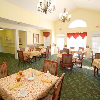 A well-lit dining area with neatly arranged tables and chairs, featuring a chandelier and decorative elements.