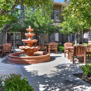 A tranquil courtyard featuring a central fountain surrounded by wooden outdoor seating and lush greenery.