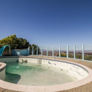 An outdoor circular pool with a slide, surrounded by a glass fence under a clear blue sky.