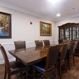 A spacious dining room with a long wooden table, surrounded by chairs and decorated with framed artwork on the walls.