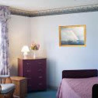 A cozy bedroom with a purple dresser, a table lamp, and wall art.