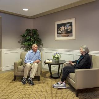Two seniors engage in a friendly conversation in a cozy living room area.