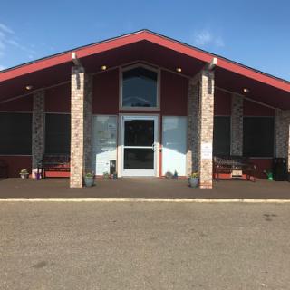 A modern building with a striking red roof and spacious entrance, surrounded by outdoor seating.