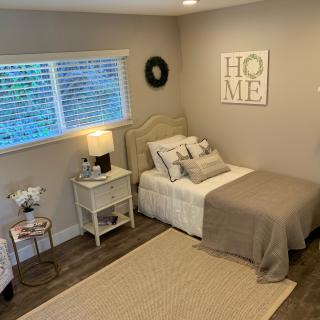 A cozy and minimalist bedroom with neutral tones, featuring a neatly made bed, nightstand with a lamp, and decorative elements.