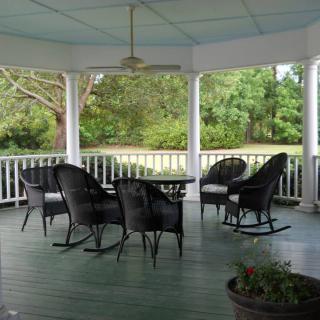 A peaceful gazebo with wicker chairs and a table, overlooking a lush garden.