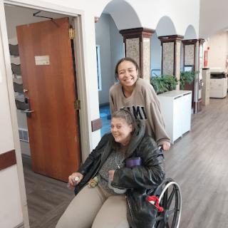 A joyful moment as one woman helps another in a wheelchair, showcasing friendship and support.