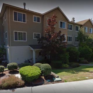 A residential building with a neatly landscaped front yard featuring bushes and a lawn.