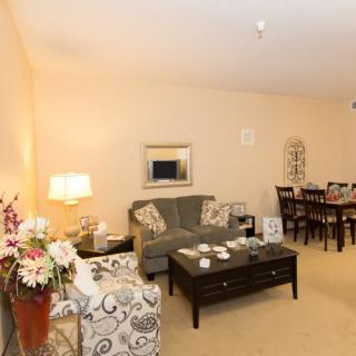 A warmly lit living room with a comfortable sofa, armchair, coffee table, and dining area.