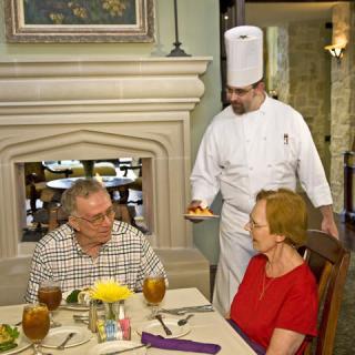 A chef presents a dish to a couple dining in a restaurant.