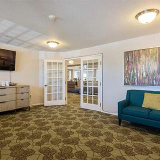 A cozy living room with a teal couch, patterned carpet, and artwork on the wall.