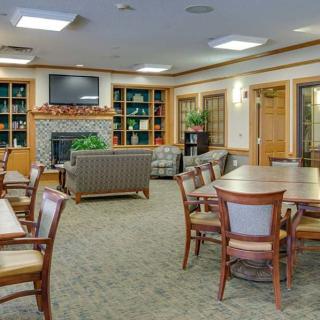 A cozy lounge area featuring tables, chairs, bookshelves, a television, and a fireplace.