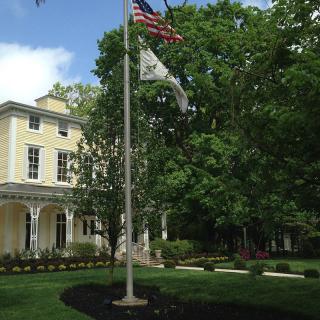 A historic house with a garden and flagpole featuring the American flag.