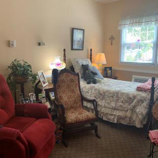 A cozy bedroom with traditional furniture, featuring an armchair, bed, and lamp near a window.