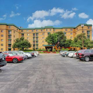 An apartment building with a parking lot filled with cars under a clear blue sky.