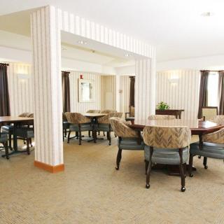 A spacious dining area with multiple tables and chairs, featuring a cozy carpeted floor and neutral-toned decor.