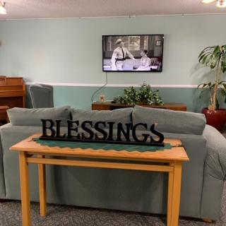 A cozy living room with a sofa, television, and decorative 'Blessings' sign.