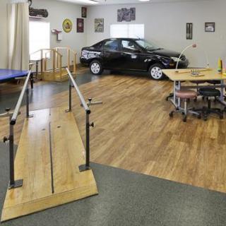 A rehabilitation center featuring a wooden ramp, exercise equipment, and an automobile for therapy purposes.