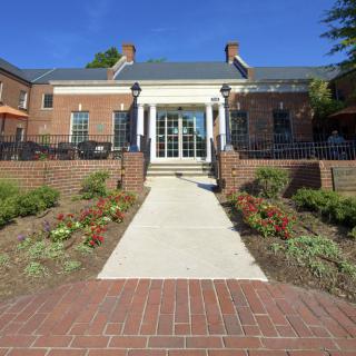 A brick building with a pathway leading to its entrance, surrounded by landscaped gardens.