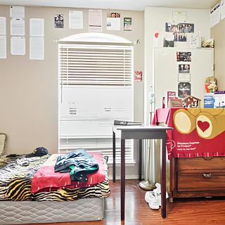 A cozy bedroom with a bed, study table, and decorative posters on the walls.