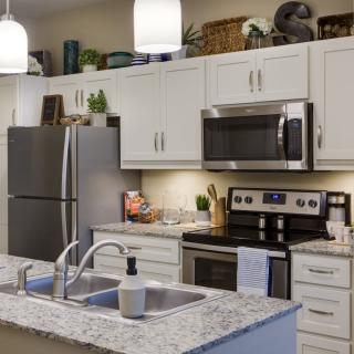 A modern kitchen with white cabinets, stainless steel appliances, and a marble countertop.