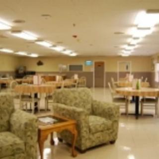 A spacious community room with armchairs and tables, featuring bright overhead lighting.