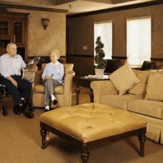 An elderly couple sitting in a cozy living room, with one person in a wheelchair.