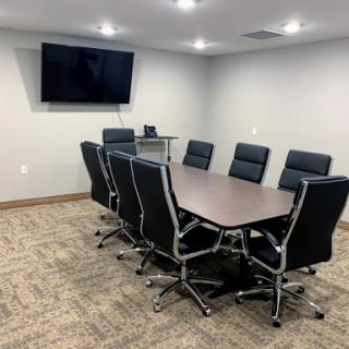 A modern meeting room equipped with a conference table, comfortable black chairs, and a wall-mounted television.