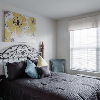 A cozy bedroom with a neatly made bed, decorative pillows, and bright natural light from the window.
