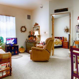 A cozy living room with a recliner chair, TV, and decor, leading into a bedroom.