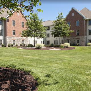 A well-maintained grassy area in front of a modern brick building with trees and landscaping.