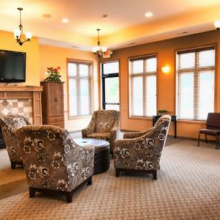 A cozy living room with floral armchairs arranged around a table, featuring a fireplace and a large window providing ample natural light.